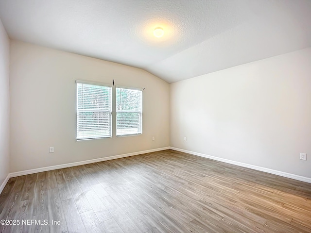 unfurnished room with lofted ceiling, baseboards, and wood finished floors