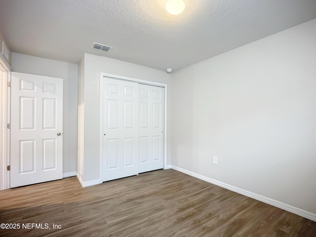 unfurnished bedroom with a closet, visible vents, baseboards, and wood finished floors