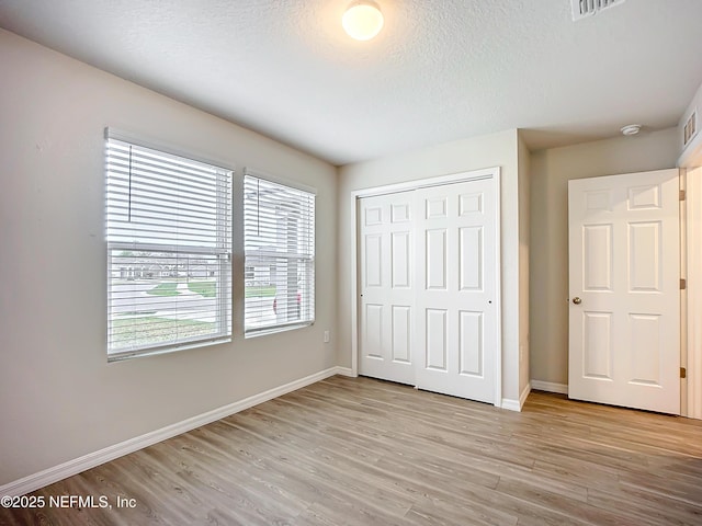 unfurnished bedroom featuring a textured ceiling, a closet, light wood-type flooring, and baseboards