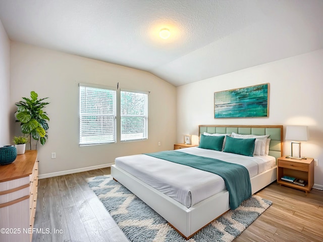 bedroom featuring lofted ceiling, light wood-style flooring, baseboards, and a textured ceiling