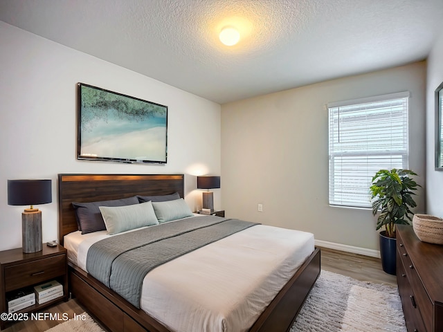 bedroom featuring a textured ceiling, baseboards, and wood finished floors