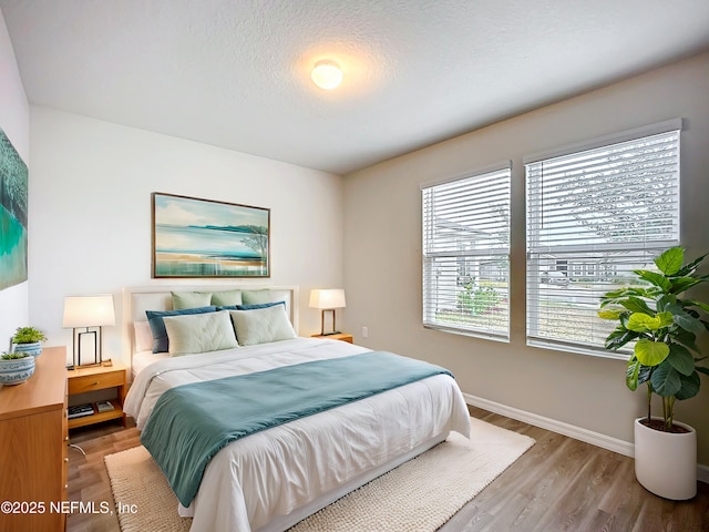 bedroom featuring a textured ceiling, baseboards, and wood finished floors