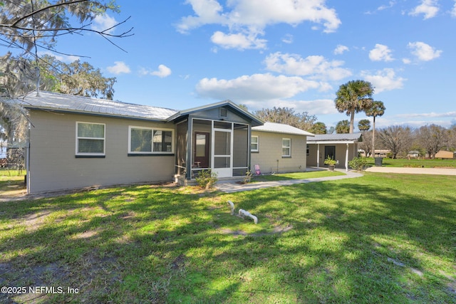 back of property with metal roof, a lawn, concrete block siding, and a sunroom