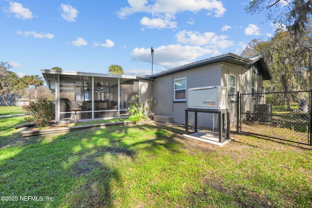 rear view of property with concrete block siding, a yard, central AC unit, a sunroom, and fence