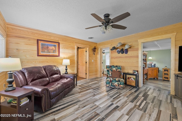 living room with a textured ceiling, ceiling fan, and wood walls