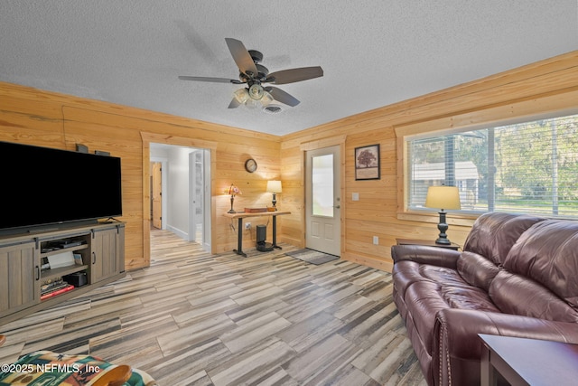 living area with wooden walls, ceiling fan, and a textured ceiling