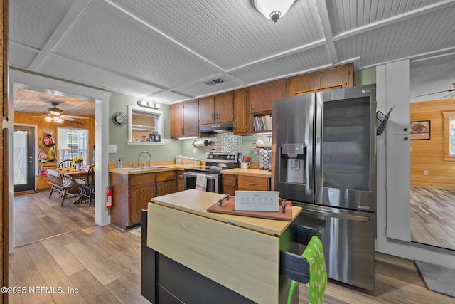 kitchen featuring light wood finished floors, stainless steel appliances, light countertops, a sink, and wooden walls