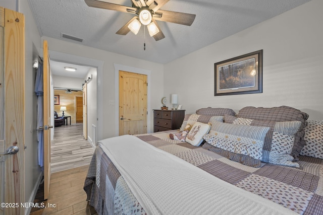 bedroom with a textured ceiling, light wood-style flooring, visible vents, and a ceiling fan