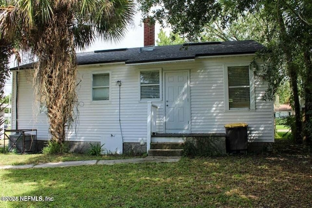 back of house with entry steps, a chimney, and a lawn