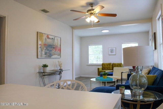 living area featuring visible vents, ceiling fan, baseboards, and wood finished floors