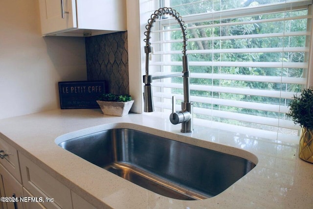 room details with white cabinetry, light stone counters, and a sink