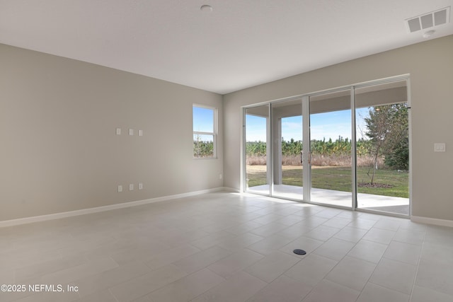 empty room with a healthy amount of sunlight, light tile patterned floors, baseboards, and visible vents