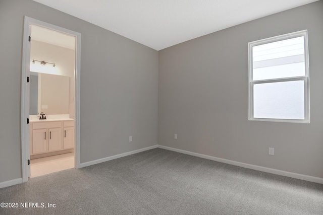 unfurnished bedroom with light carpet, a sink, baseboards, and ensuite bathroom