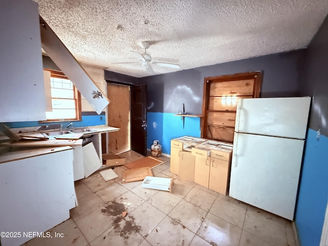 kitchen with light countertops, freestanding refrigerator, ceiling fan, a textured ceiling, and a sink