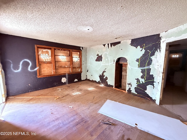 empty room with arched walkways, a textured ceiling, and wood finished floors