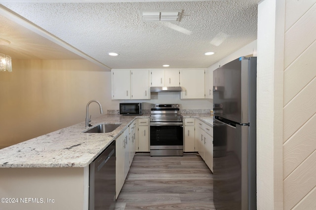 kitchen featuring appliances with stainless steel finishes, white cabinets, a sink, light stone countertops, and a peninsula