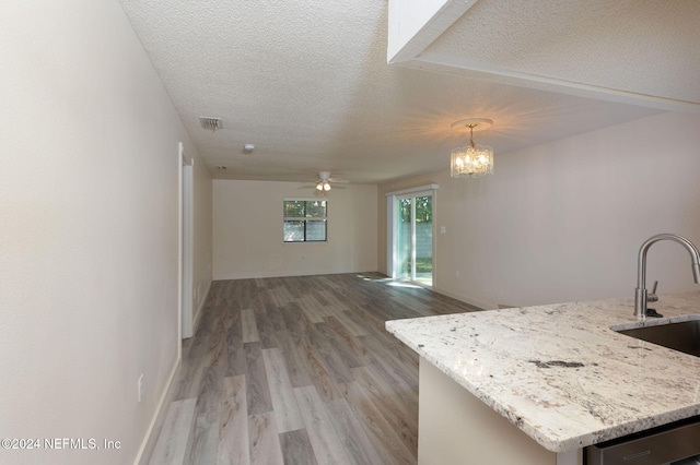 kitchen featuring hanging light fixtures, light wood-style floors, open floor plan, a textured ceiling, and light stone countertops