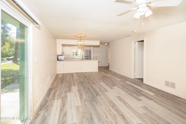 unfurnished living room featuring light wood finished floors, baseboards, visible vents, and a textured ceiling