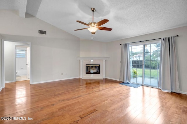 unfurnished living room with a glass covered fireplace, vaulted ceiling, visible vents, and light wood-type flooring