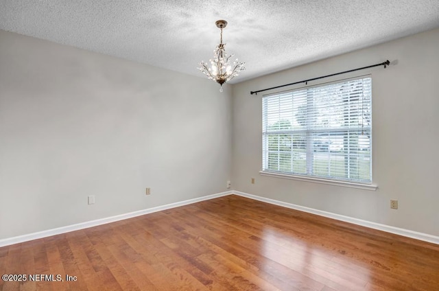 empty room featuring a chandelier, a textured ceiling, baseboards, and wood finished floors