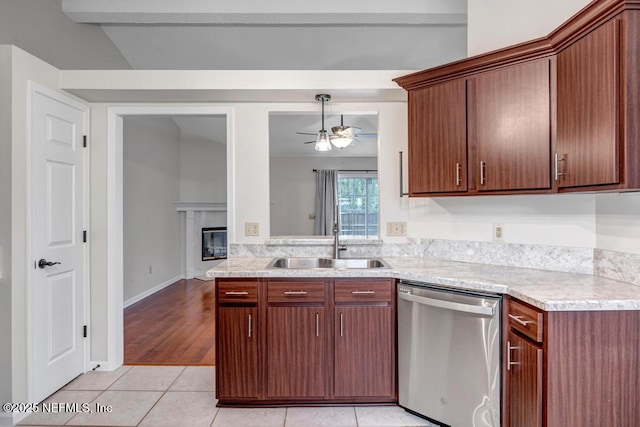 kitchen with a sink, a glass covered fireplace, light tile patterned flooring, light countertops, and dishwasher