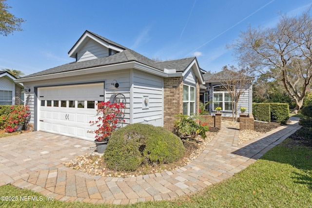 view of front facade with a garage, a shingled roof, and brick siding