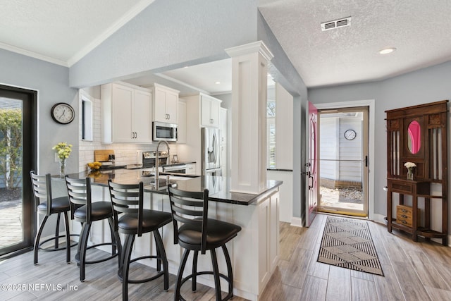 kitchen featuring tasteful backsplash, dark countertops, appliances with stainless steel finishes, a kitchen breakfast bar, and a peninsula