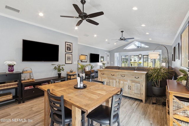 dining space with lofted ceiling with skylight, crown molding, visible vents, and light wood-style floors