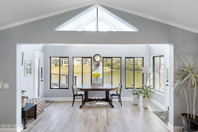 dining space featuring ornamental molding, vaulted ceiling with skylight, light wood-style floors, and baseboards