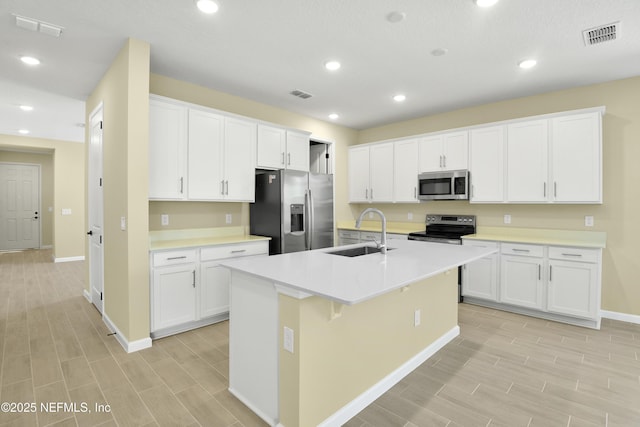 kitchen with stainless steel appliances, a sink, visible vents, light countertops, and an island with sink