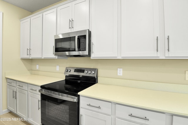 kitchen featuring stainless steel appliances, light countertops, white cabinets, and light wood-style flooring