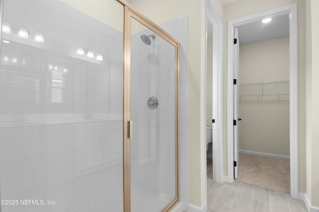 full bath featuring a stall shower, baseboards, a spacious closet, and toilet