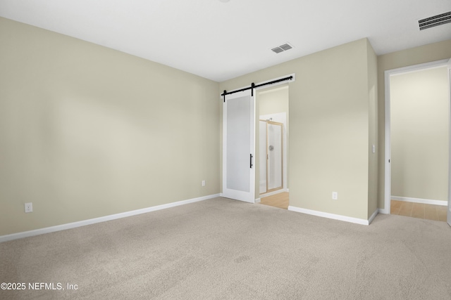 unfurnished bedroom featuring light carpet, a barn door, visible vents, and baseboards