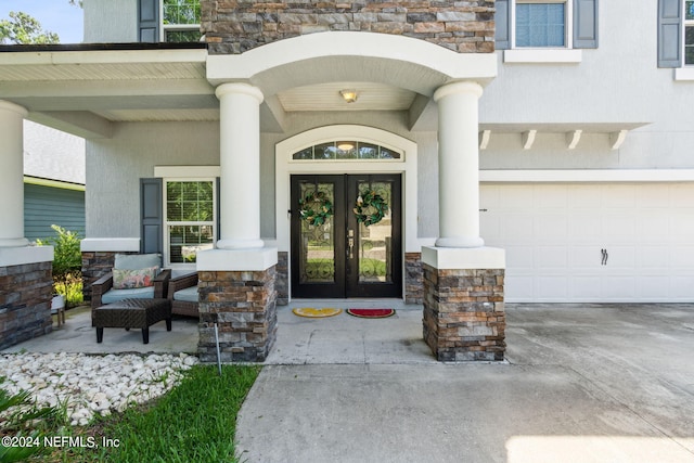 doorway to property featuring french doors, stucco siding, concrete driveway, an attached garage, and stone siding