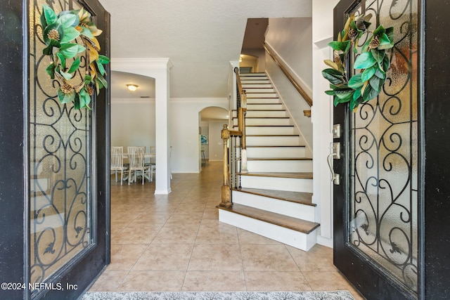 entryway featuring light tile patterned floors, baseboards, arched walkways, stairway, and crown molding