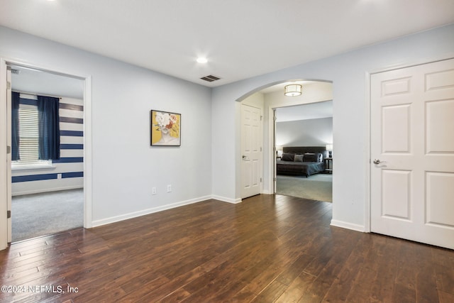 empty room featuring arched walkways, wood-type flooring, visible vents, and baseboards