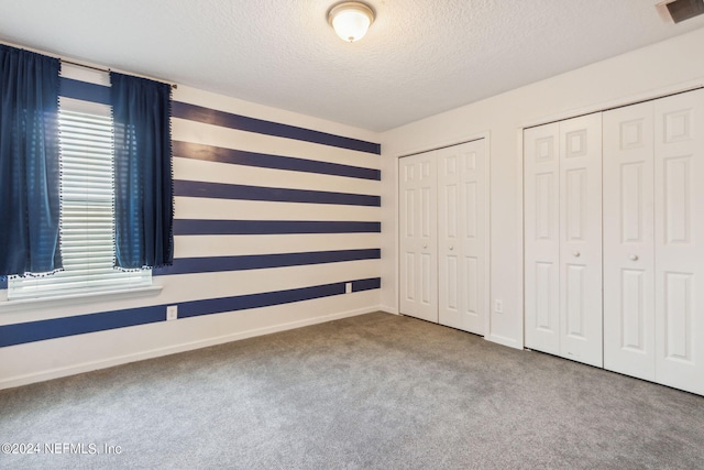 unfurnished bedroom with multiple closets, visible vents, carpet flooring, a textured ceiling, and baseboards