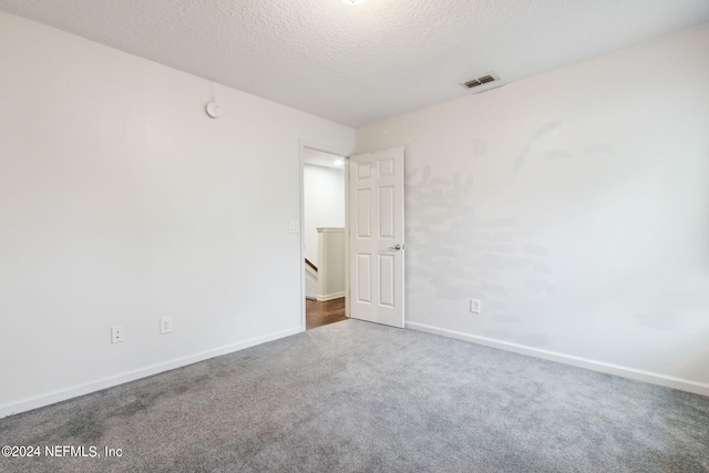 spare room featuring carpet floors, baseboards, visible vents, and a textured ceiling