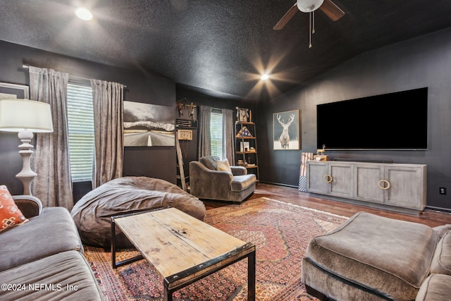 living area featuring a ceiling fan, vaulted ceiling, a textured ceiling, and wood finished floors