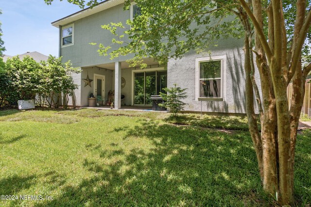 rear view of house featuring a patio area, a lawn, and stucco siding