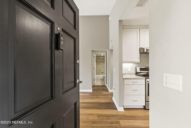 hallway with light wood finished floors, visible vents, and baseboards