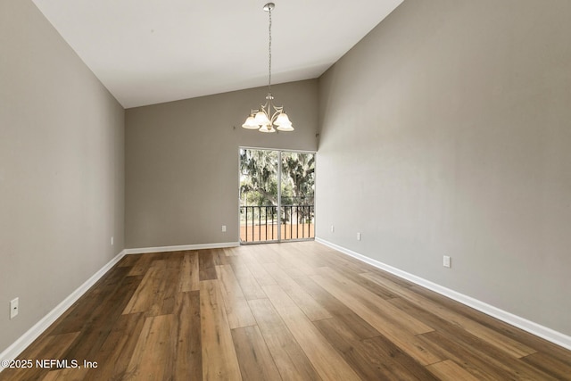 spare room featuring dark wood-style floors, baseboards, lofted ceiling, and an inviting chandelier