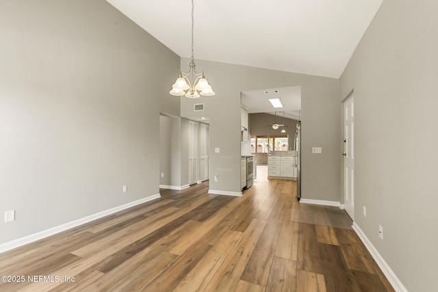 interior space with lofted ceiling, ceiling fan with notable chandelier, visible vents, baseboards, and wood-type flooring