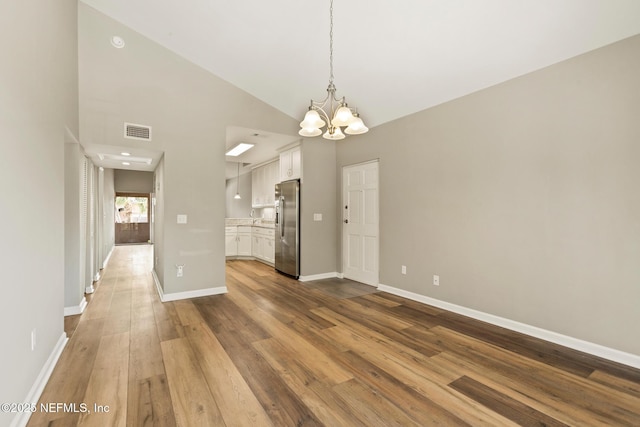 unfurnished dining area featuring dark wood finished floors, a notable chandelier, visible vents, vaulted ceiling, and baseboards