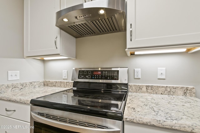 kitchen featuring electric range, light stone countertops, white cabinets, and under cabinet range hood