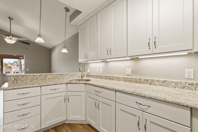 kitchen with decorative light fixtures, a peninsula, vaulted ceiling, white cabinetry, and a sink