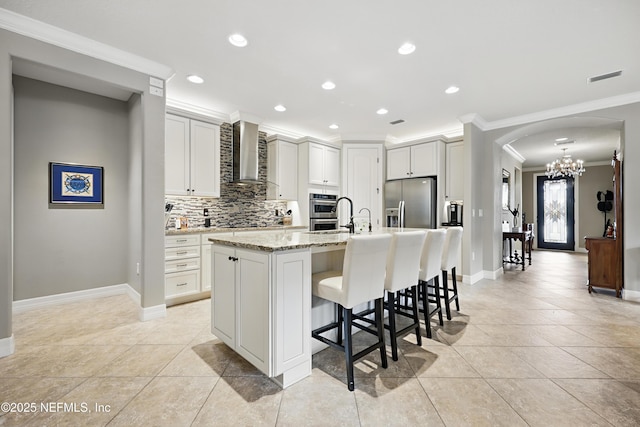 kitchen featuring tasteful backsplash, arched walkways, appliances with stainless steel finishes, crown molding, and wall chimney range hood