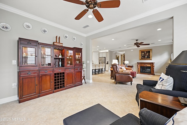 living room featuring visible vents, baseboards, a glass covered fireplace, ornamental molding, and recessed lighting