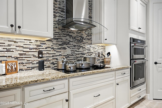 kitchen with black electric stovetop, light tile patterned floors, tasteful backsplash, stainless steel double oven, and wall chimney range hood