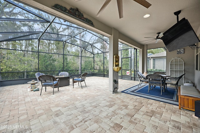 view of patio with a lanai, outdoor dining space, a ceiling fan, and an outdoor living space with a fire pit